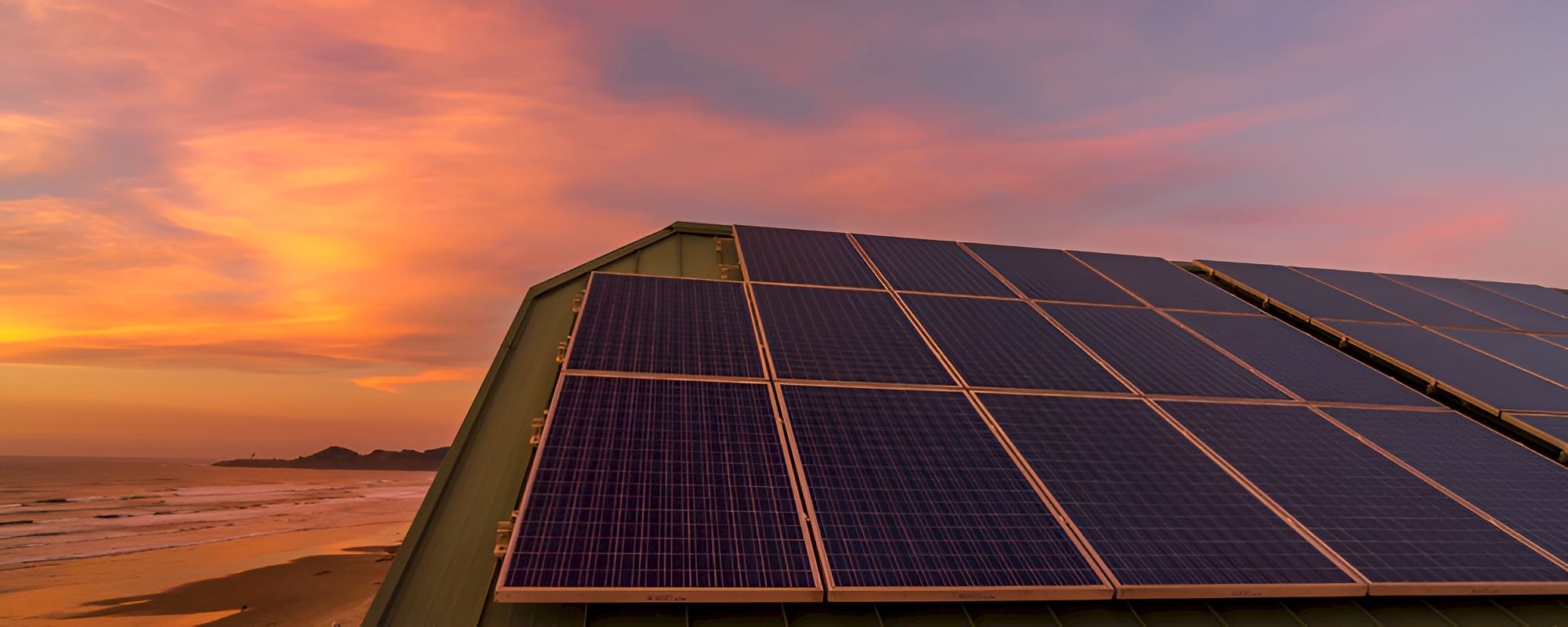Solar panels line a rooftop at sunset, glowing orange skies over a calm shoreline.
