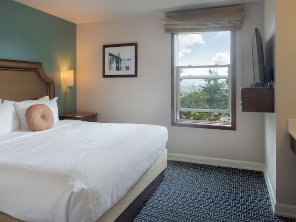 A tidy hotel room with a large bed, teal accent wall, nightstand, framed art, window view, and a wall-mounted desk; bright and airy.
