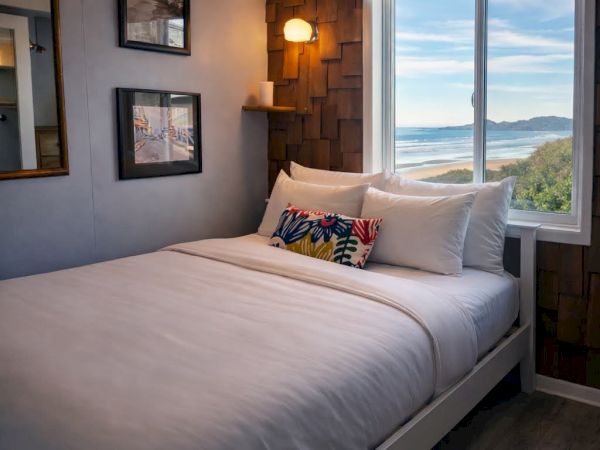 Cozy hotel room with a white bed, wall art, a window view of water and hills, and warm bedside lighting. End.