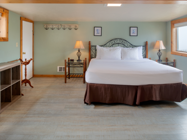 A large hotel room with a king bed, two nightstands, lamps, and a wrought-iron headboard, soft blue walls, wooden accents, and plenty of natural light.