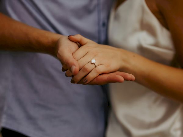 Two people are holding hands; one wears an engagement ring, suggesting a wedding or vow moment.