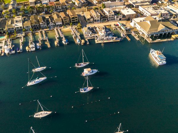 Aerial view of a coastal town with a marina full of boats, a pier extending into calm blue water, and an orderly grid of houses along the shore.