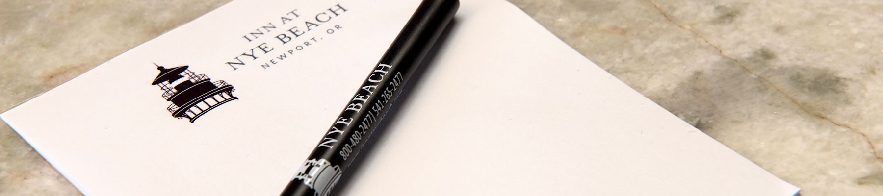 A white card or envelope with a black pen resting on top, on a light stone surface. The card has a small logo and text.