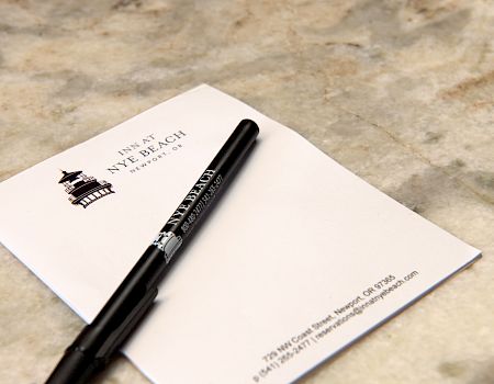 A white card or envelope with a black pen resting on top, on a light stone surface. The card has a small logo and text.