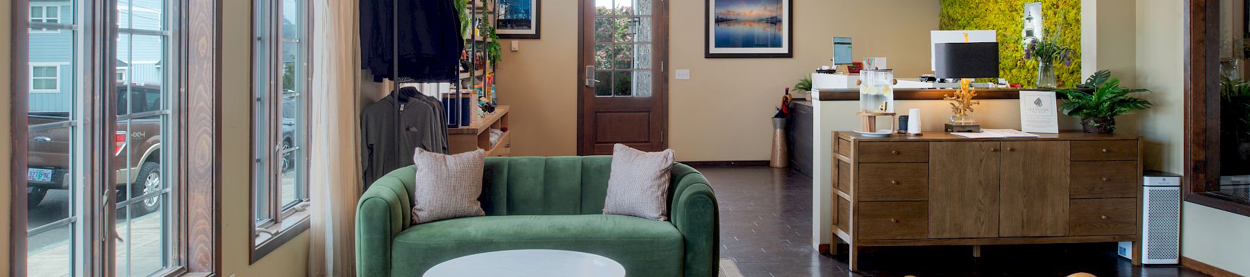 A stylish reception area with a green sofa, two orange leather chairs, round coffee tables, and a small white nesting table, plus a reception desk in the background.