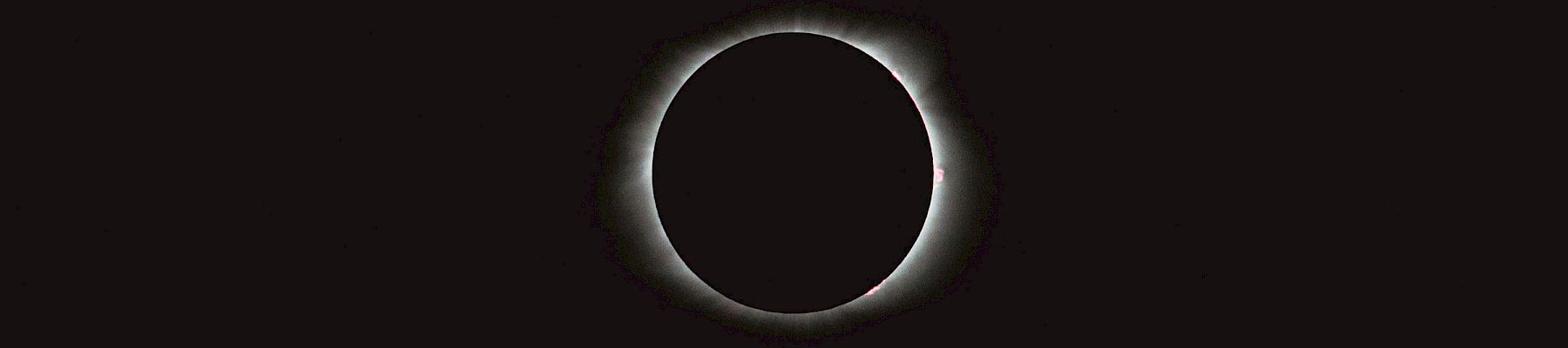A dark background with a bright ring around a nearly black circle, resembling a solar eclipse silhouette, centered and minimalist.