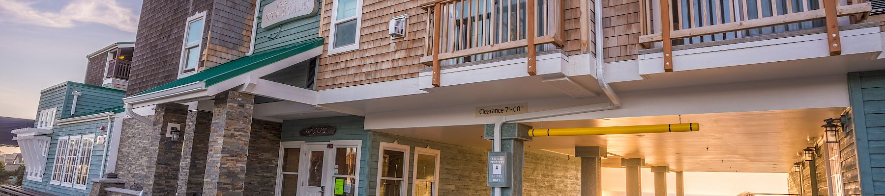 A seaside motel with balconies, brick facade, covered walkway, and sunset glow at the entrance.