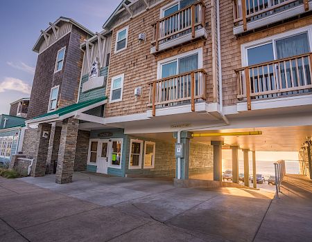 A seaside motel with balconies, brick facade, covered walkway, and sunset glow at the entrance.
