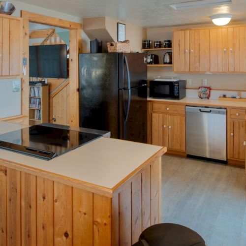 A cozy wood-paneled kitchen with a central island, white countertops, fridge, stove, microwave, dishwasher, and warm cabin vibes.