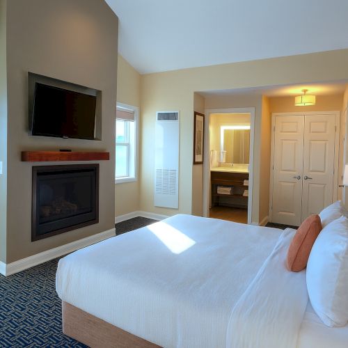 A cozy hotel room with a large bed, soft lighting, a desk, bedside lamps, and a windowed seating area.