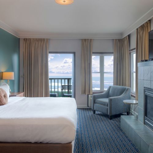 A modern hotel room with two single beds, blue and white decor, hanging lamp, large window with sheer curtains, and a desk near the window.