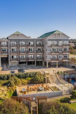 A row of three-story beach houses with balconies, a fenced yard, and a pool under construction in the foreground, set on a sunny coastal lot.