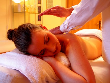 A woman receives a relaxing spa massage while lying face down on a towel, with a therapist&rsquo;s hand gently working on her back.