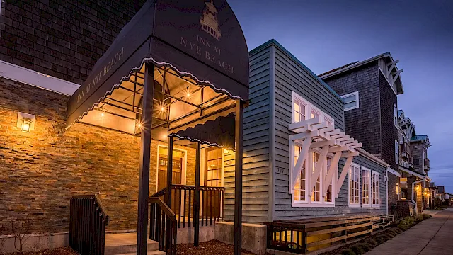 A cozy storefront with warm lights, brick and siding exterior, a welcoming awning, and a wooden staircase along a quiet street at dusk.